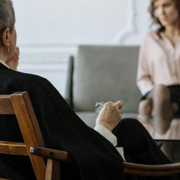 A therapist sits in a chair while a woman talks across from them.