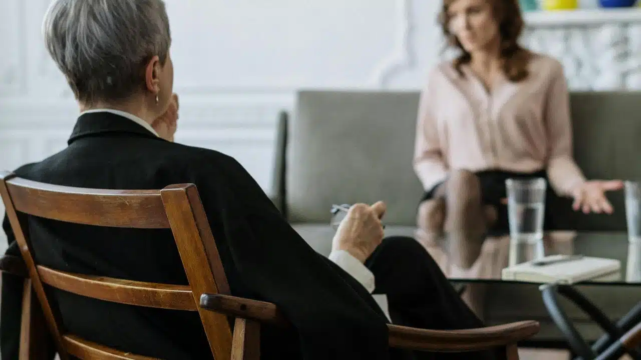 A therapist sits in a chair while a woman talks across from them.