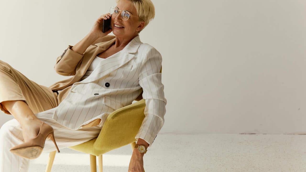 A woman in a stylish suit sitting on a chair and talking on the phone.