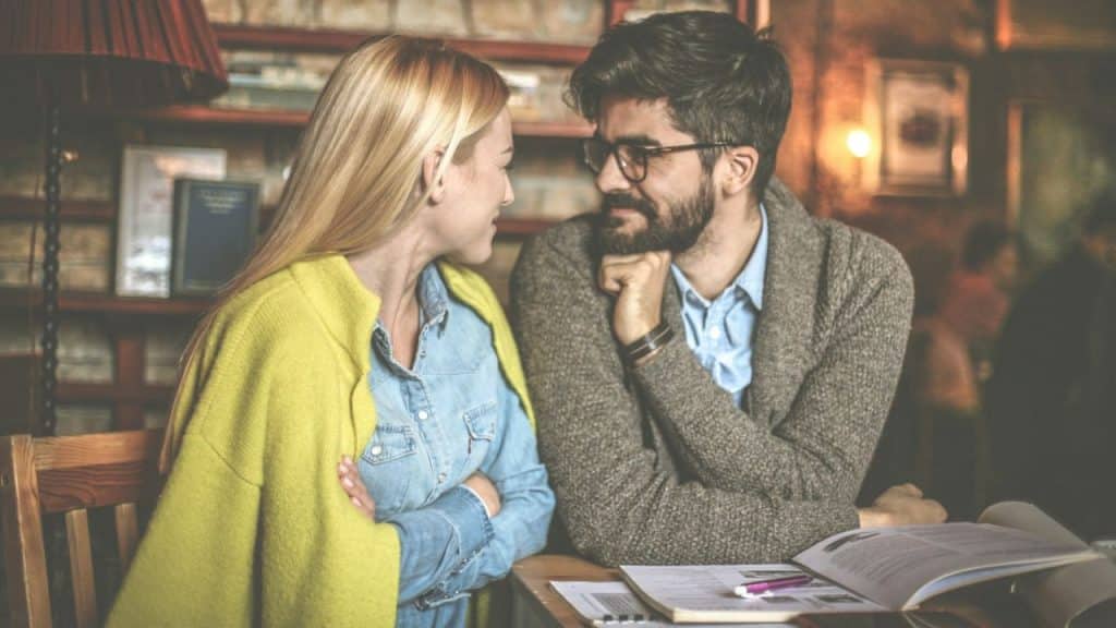 Woman with blonde hair and man with beard looking at each other in a cafe.
