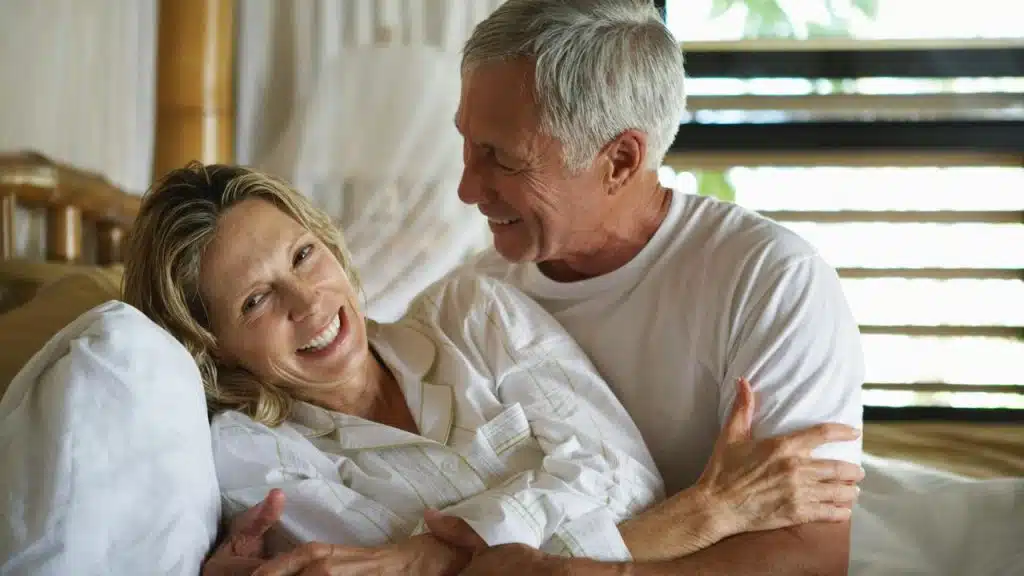 An older couple smiling and cuddling together in bed.