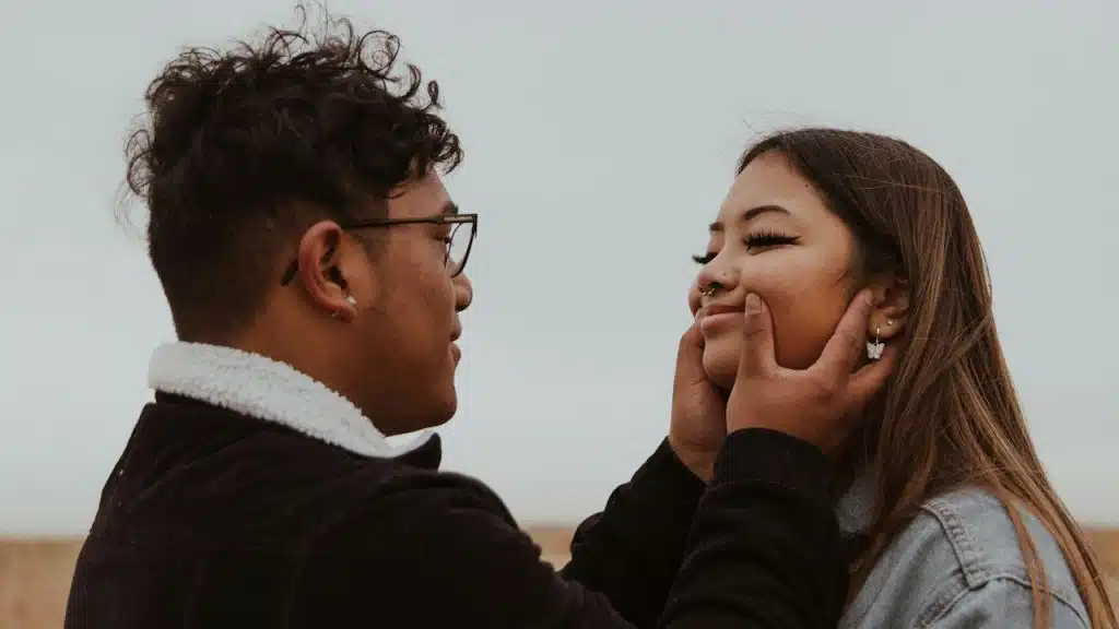 A man wearing glasses pulling on a woman’s lips to make her smile.