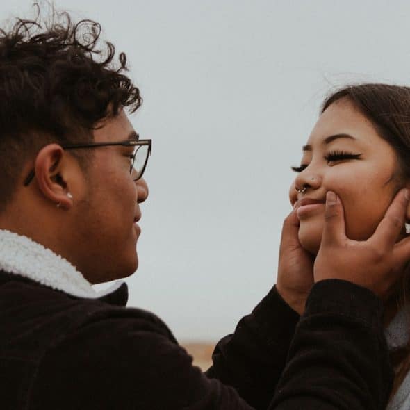 A man wearing glasses pulling on a woman’s lips to make her smile.