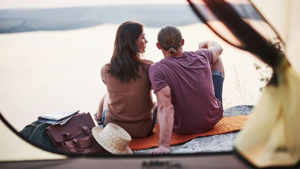 A man and woman sit on a rock together, looking out over a body of water.