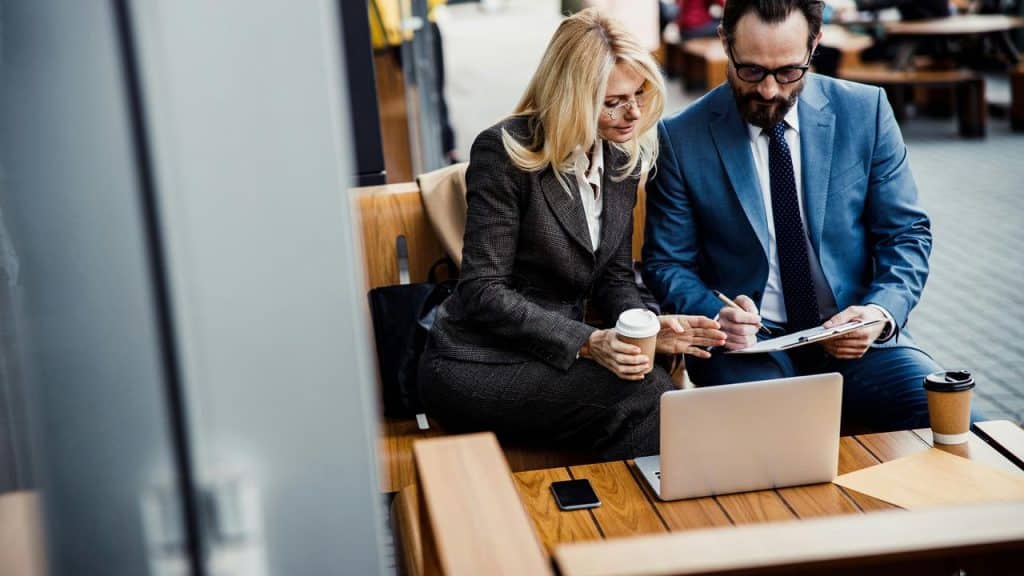 A business couple reviewing documents and working on a laptop outdoors.