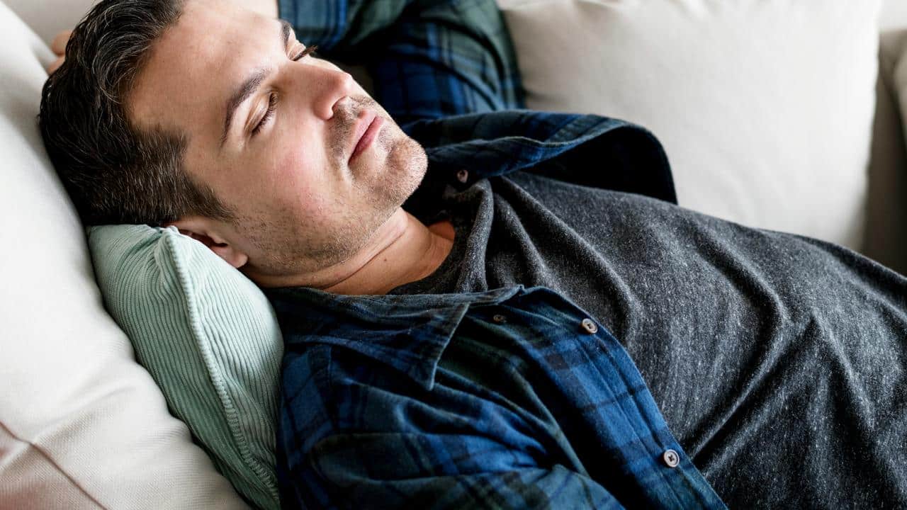 A man resting on a couch with his head on a cushion.