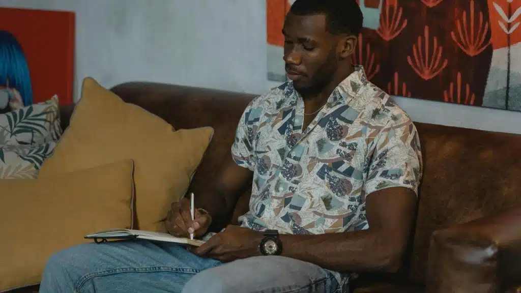 A man sitting on a couch and writing in a notebook.