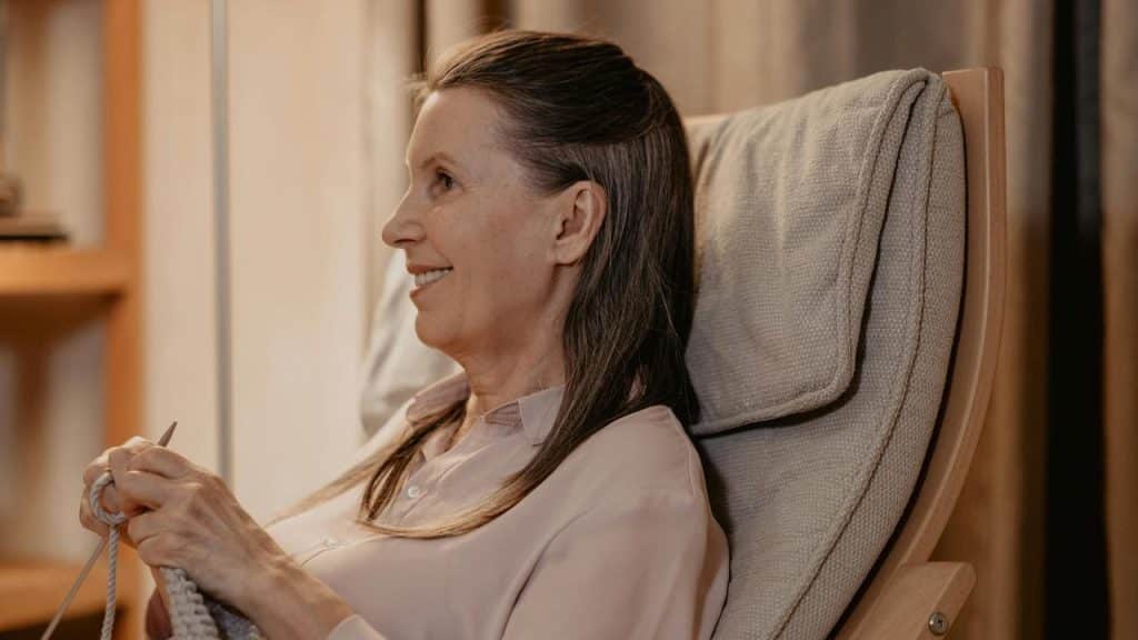 A woman sitting in a chair and smiling while knitting.