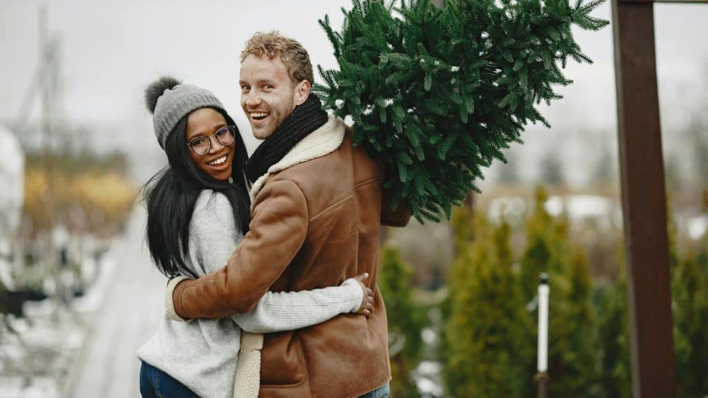 A happy couple carrying a small Christmas tree.