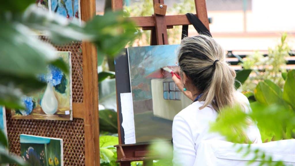 A woman with her hair in a ponytail painting outdoors.