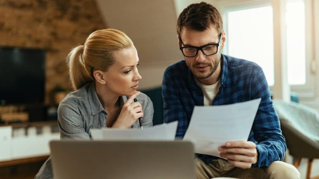 A focused couple reviews documents together, with a laptop in the foreground.