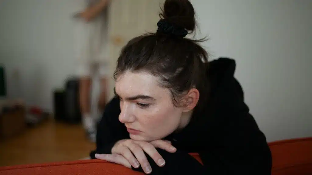 Woman with dark hair in a bun resting her chin on her hands, looking down sadly.