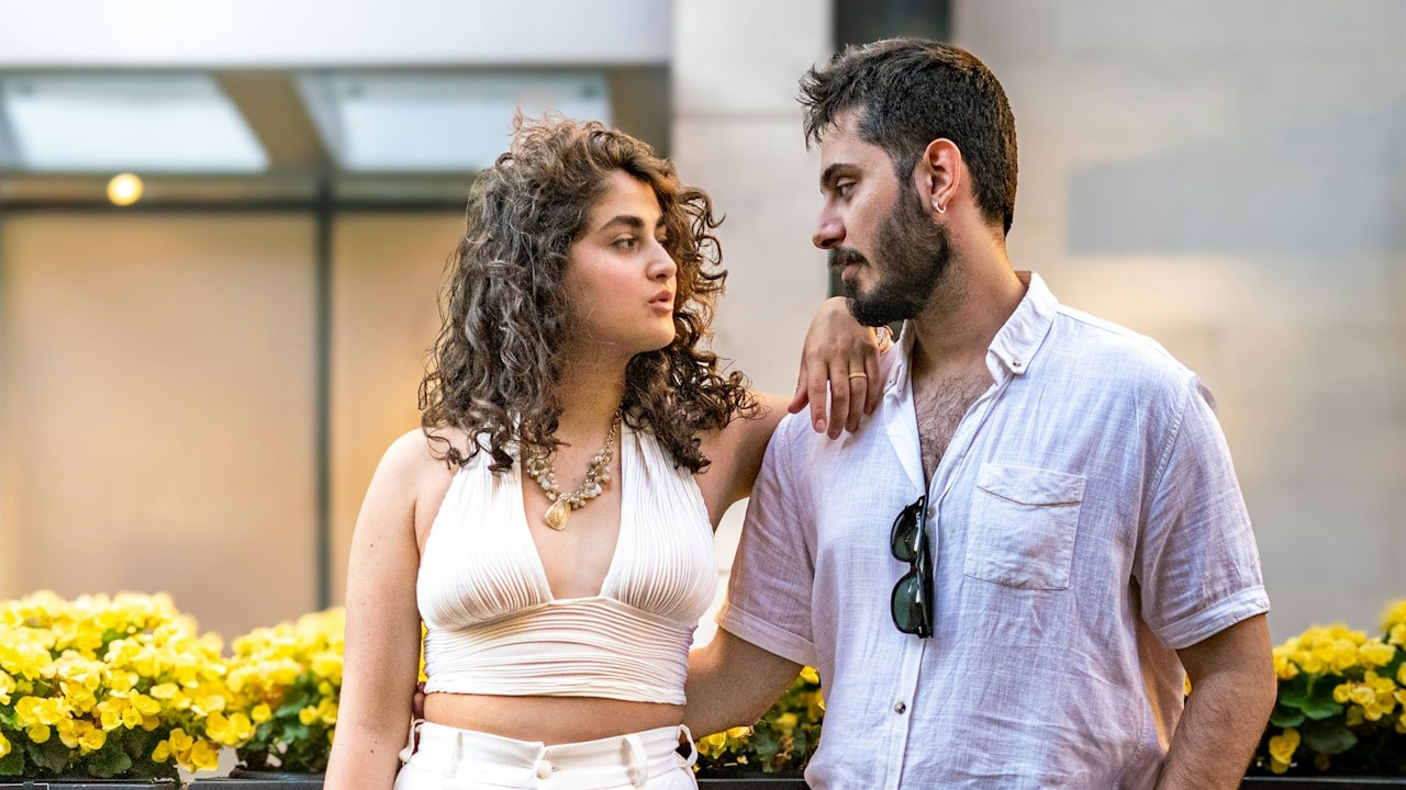 A couple poses together outdoors, looking at each other.