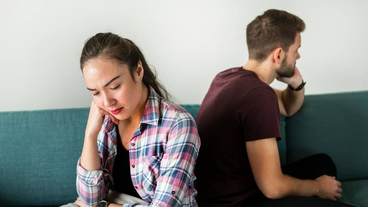A man and woman sit back-to-back on a blue couch after an argument.
