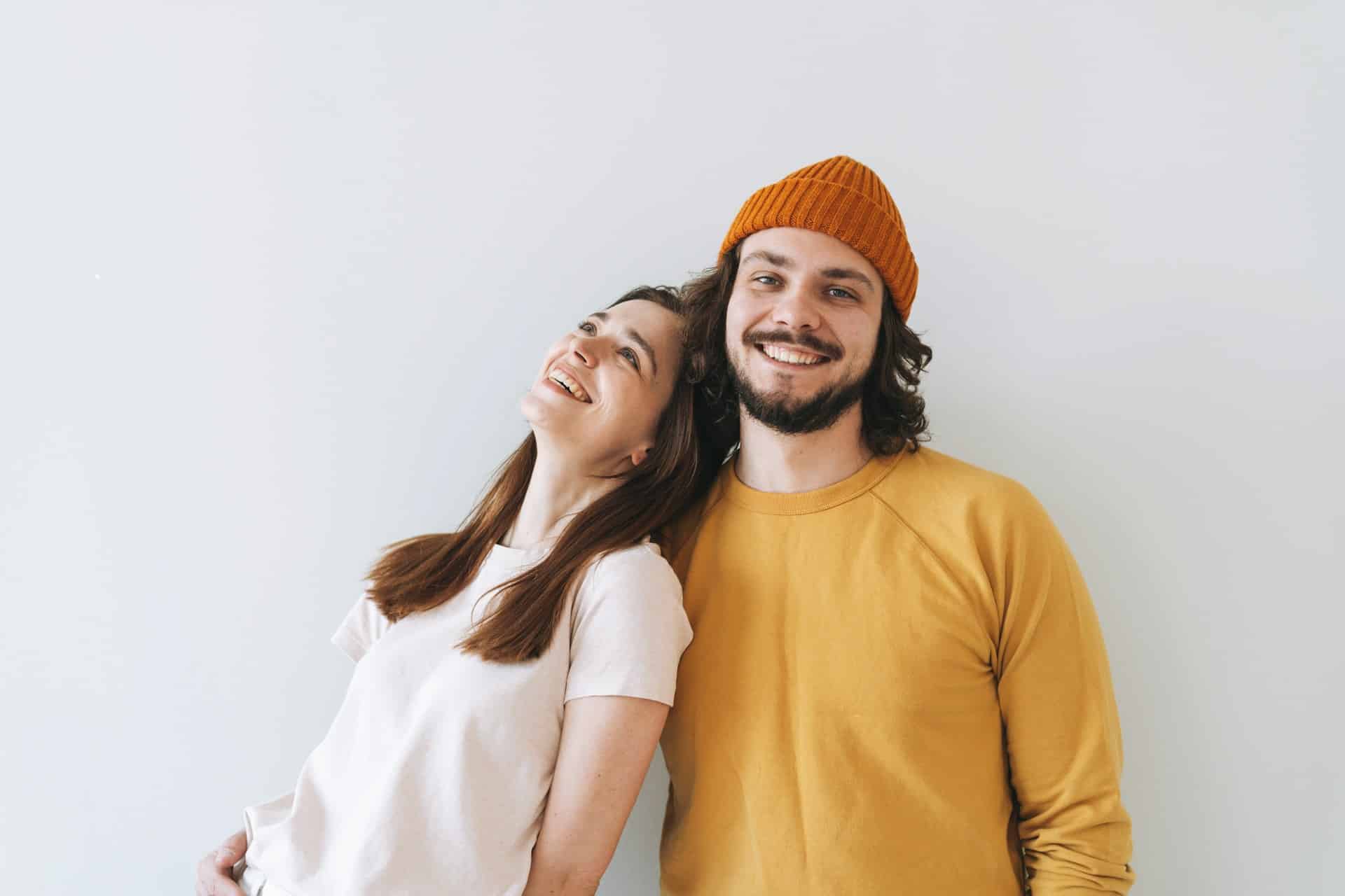A couple smiling while standing in front of a gray wall.