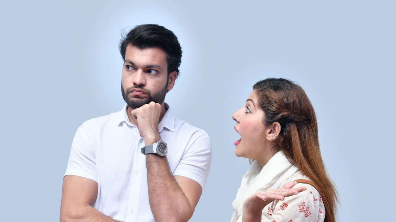 A bearded man looking to the side with his fist resting on his chin while a woman nags him. 
