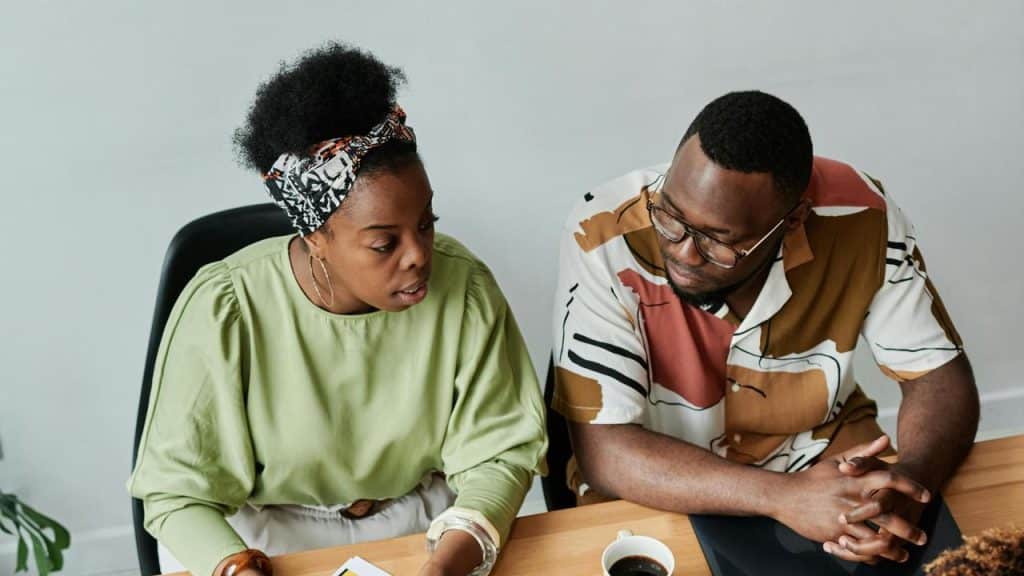 A man and a woman sitting at a table talking while looking at papers.
