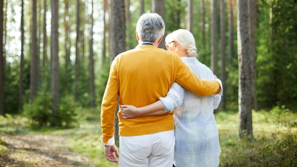 A mature couple standing in a forest with their arms around each other.