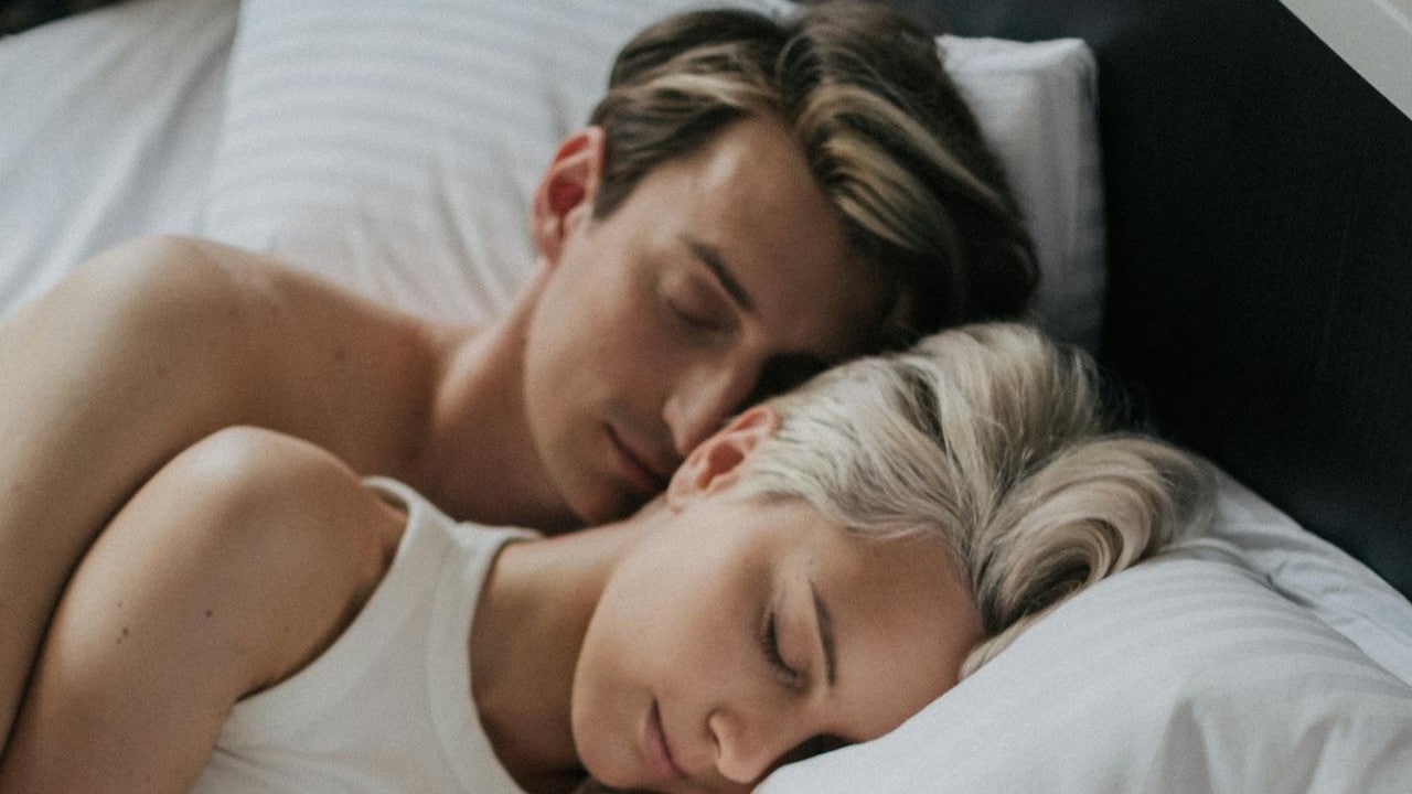 A couple sleeping close together in a bed with white sheets and pillows.