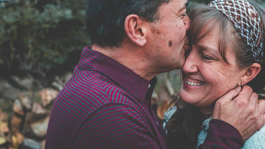 A couple smiling as the man kisses the woman on the cheek.