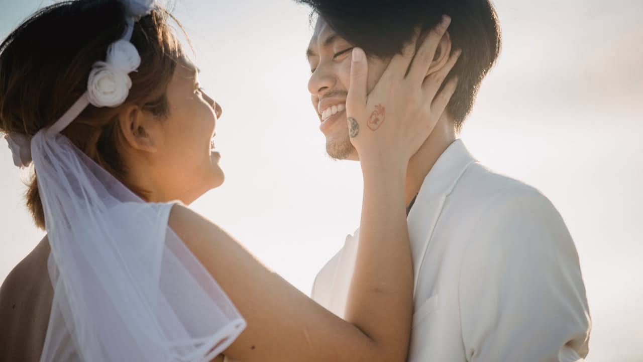 A happy couple smiling and touching faces outdoors in soft light.