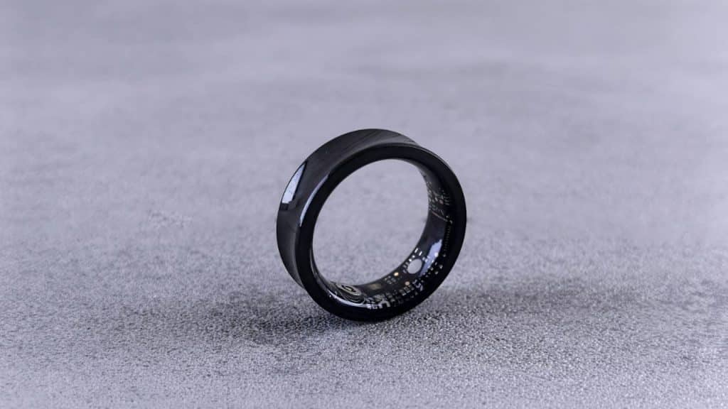 A shiny black smart ring with internal circuitry visible is upright on a gray surface.