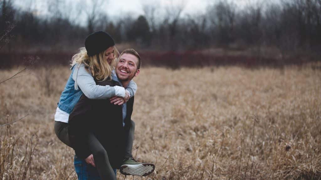 A man giving a woman a piggyback ride in a field of tall, dry grass.