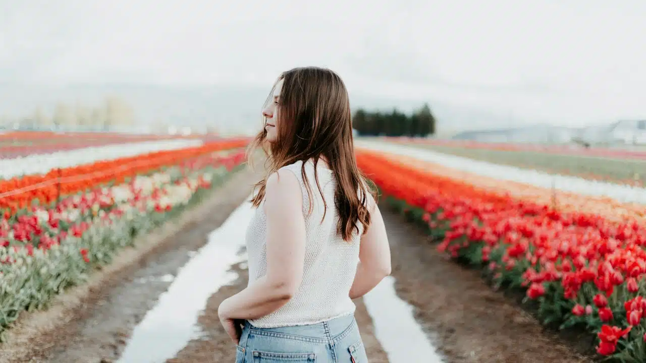 A woman wearing white tops is standing in a garden of flowers.