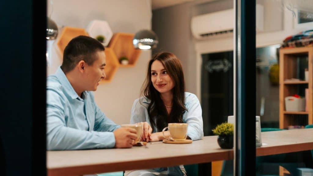 Man and woman smiling at each other while having coffee at a cafe table.
