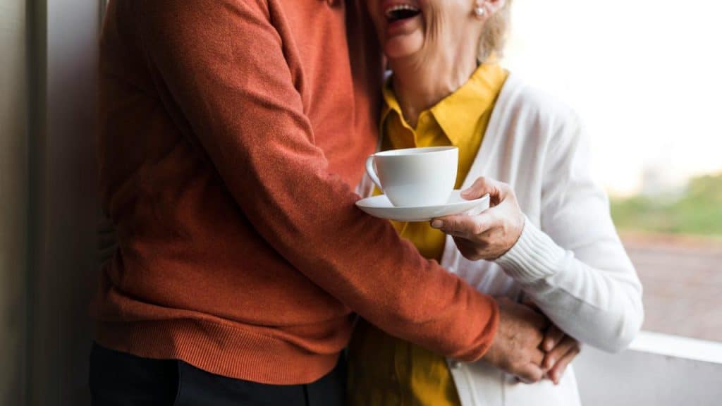 A joyful older couple embracing while holding a cup of coffee.