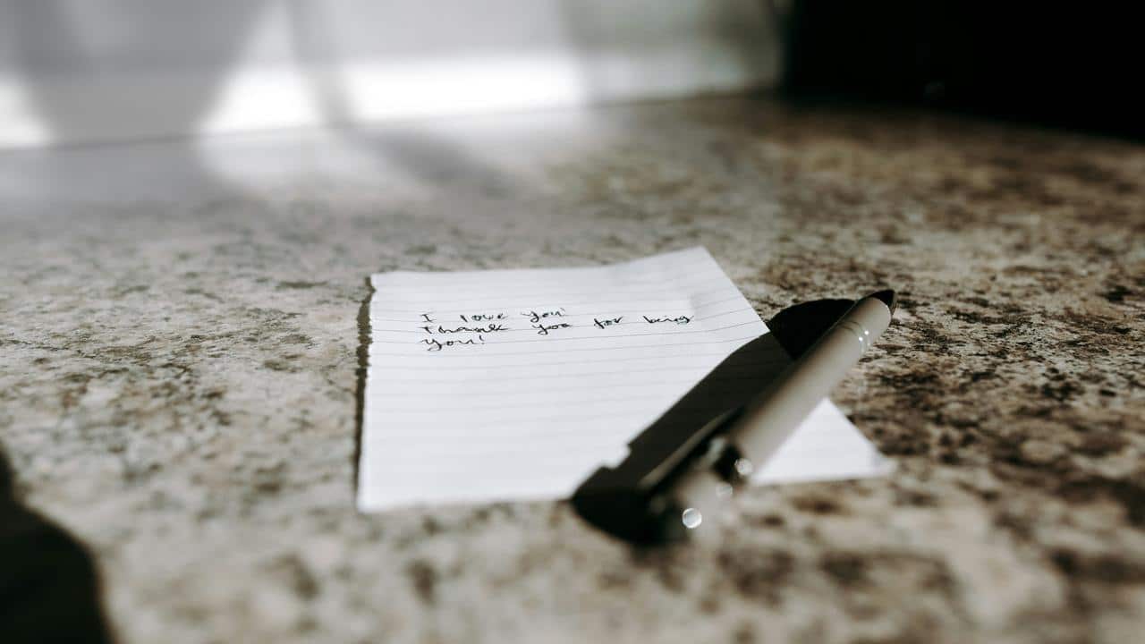 A handwritten love note on a countertop beside a pen.