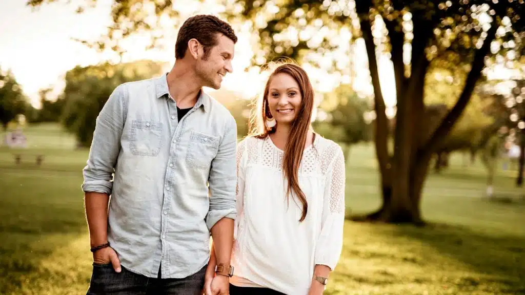 A smiling couple walking through a park while holding hands.