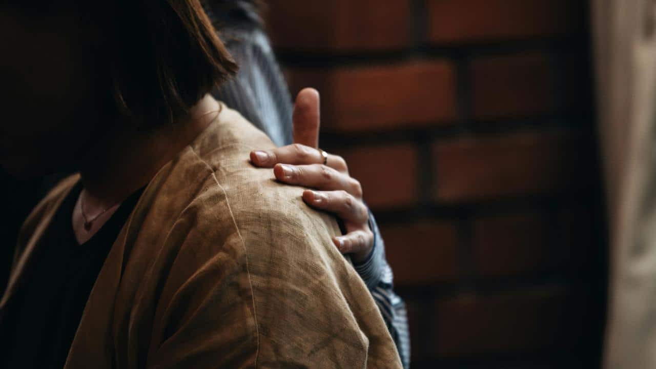 A person comforting another by placing a hand on their shoulder.
