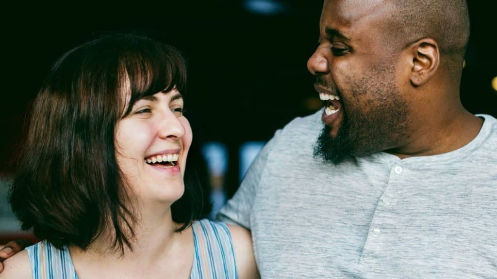 Smiling African American man embracing and laughing with a Caucasian woman outdoors.