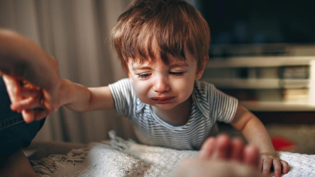 A crying baby reaching toward an adult’s hand.