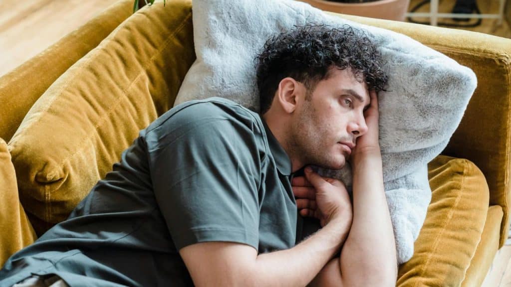 A man lying on a couch resting his head on a pillow and staring ahead.
