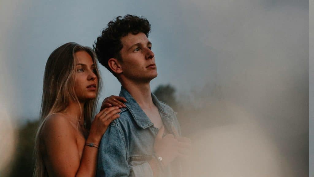 A side view of a young couple on a walk in nature at sunset in the countryside, standing.
