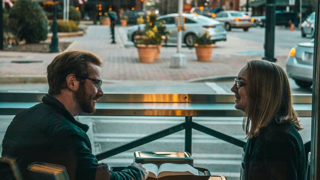 A man and a woman talking while sitting at a table in the open air.