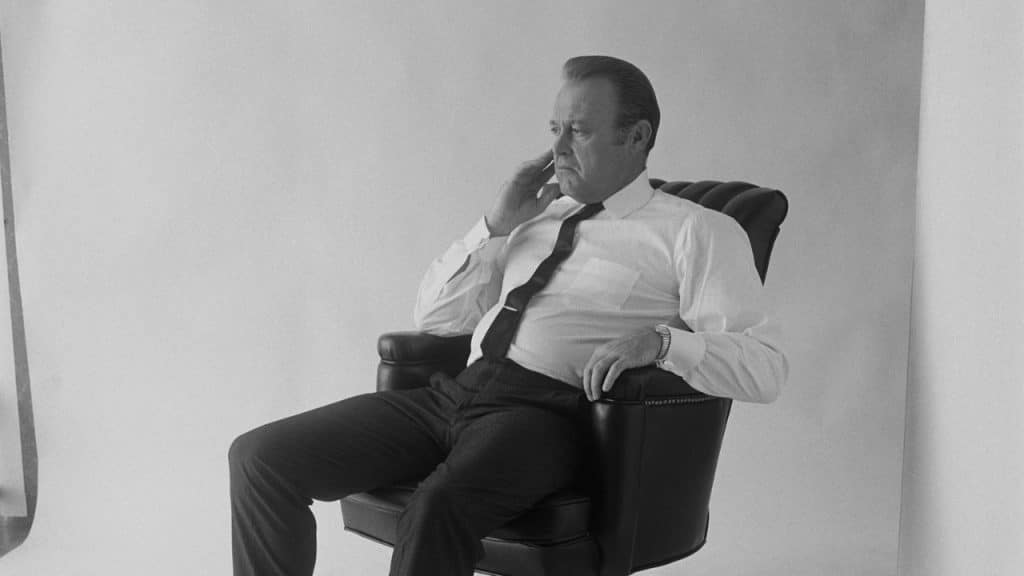 Black and white photo of a man in a shirt and tie sitting in a black chair.