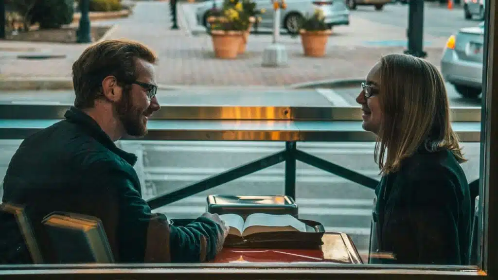 Two people smiling, looking at each other across a table with an open book.