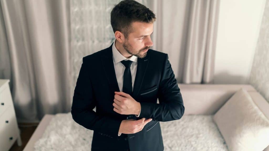 Man in a black suit adjusting his cufflink while looking away from the camera.