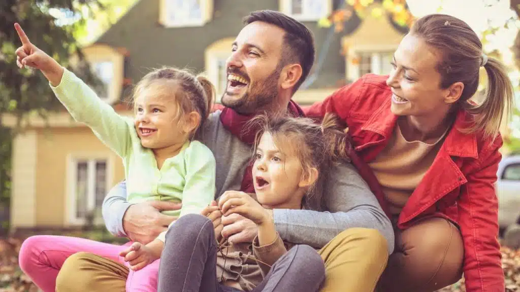 Father pointing and smiling while sitting with two young daughters and a woman.