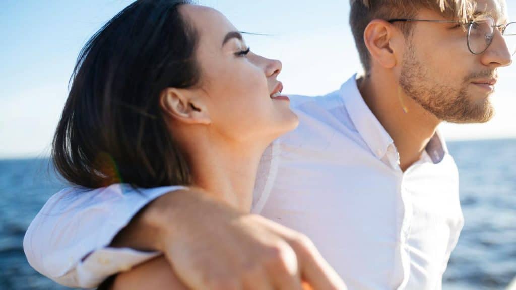 A couple standing close together by the sea, enjoying the ocean breeze.