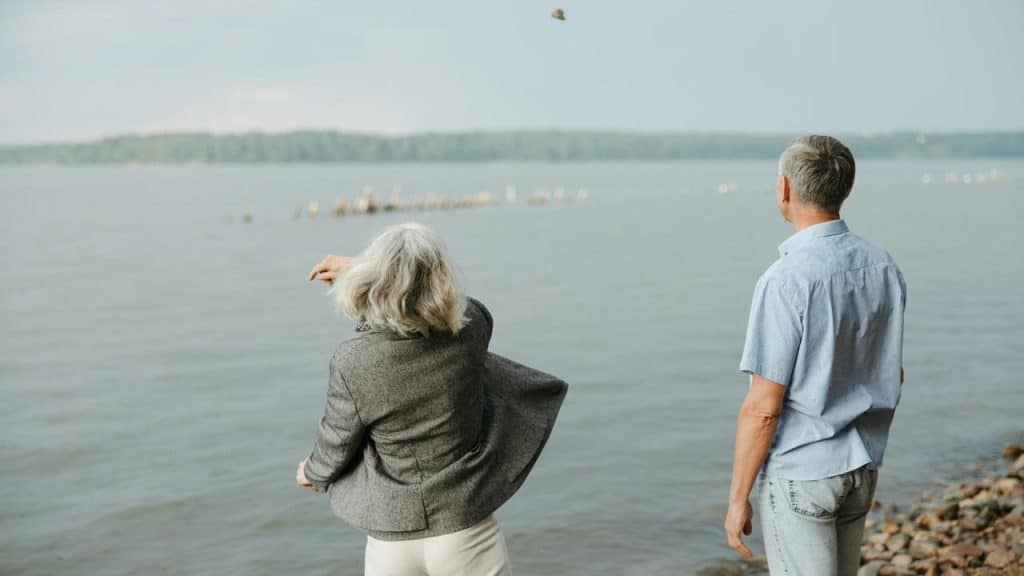 A senior couple standing by the water, watching the waves.