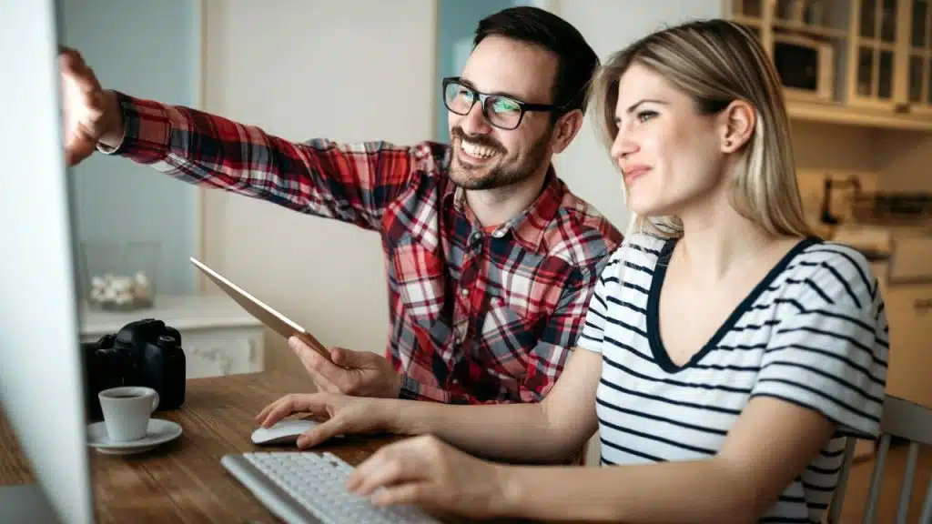 A man and woman sit at a desk while looking at a large computer screen together.