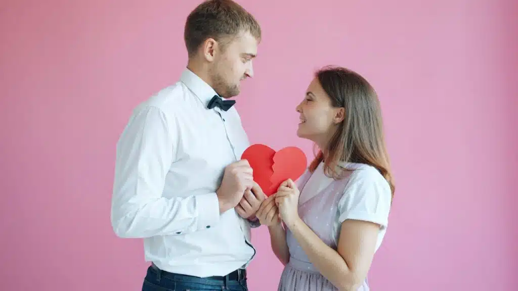 A couple holding two halves of a cardboard heart, which they are connecting.