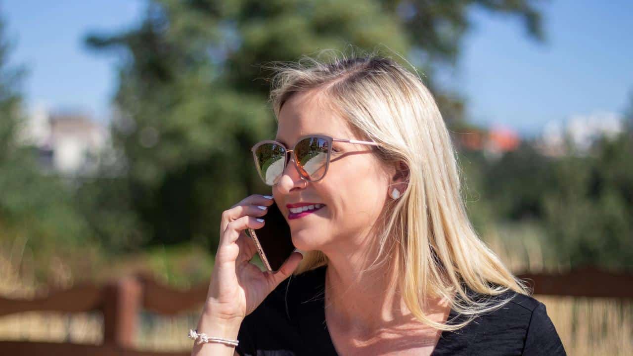 A woman wearing sunglasses talking on the phone outdoors.