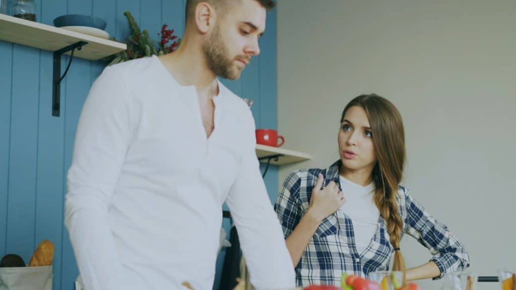 A woman in a plaid shirt looks toward a man wearing a white long-sleeved shirt.