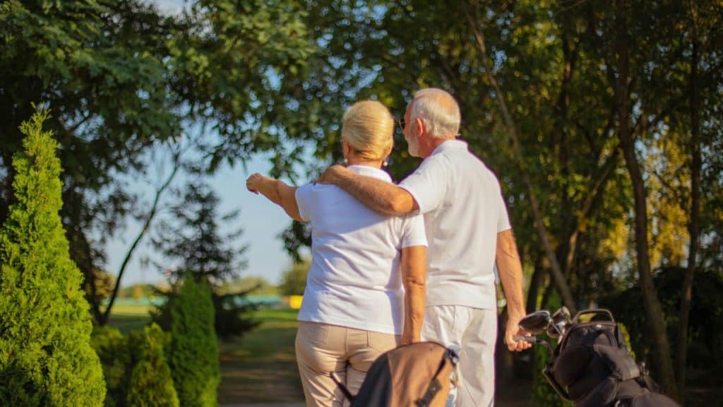 An elderly couple walking together on a golf course.