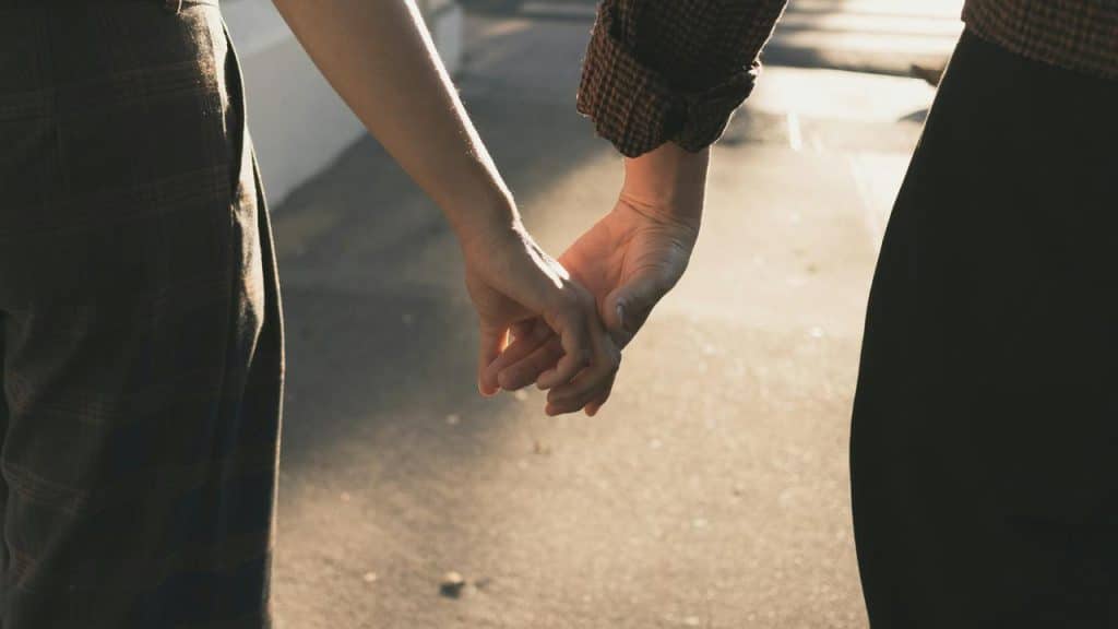 A couple holding hands while walking in soft sunlight.